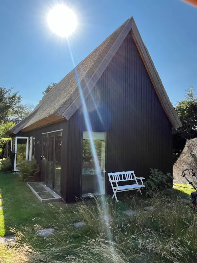 Sort træhus med stråtag og bænk ved gavlen